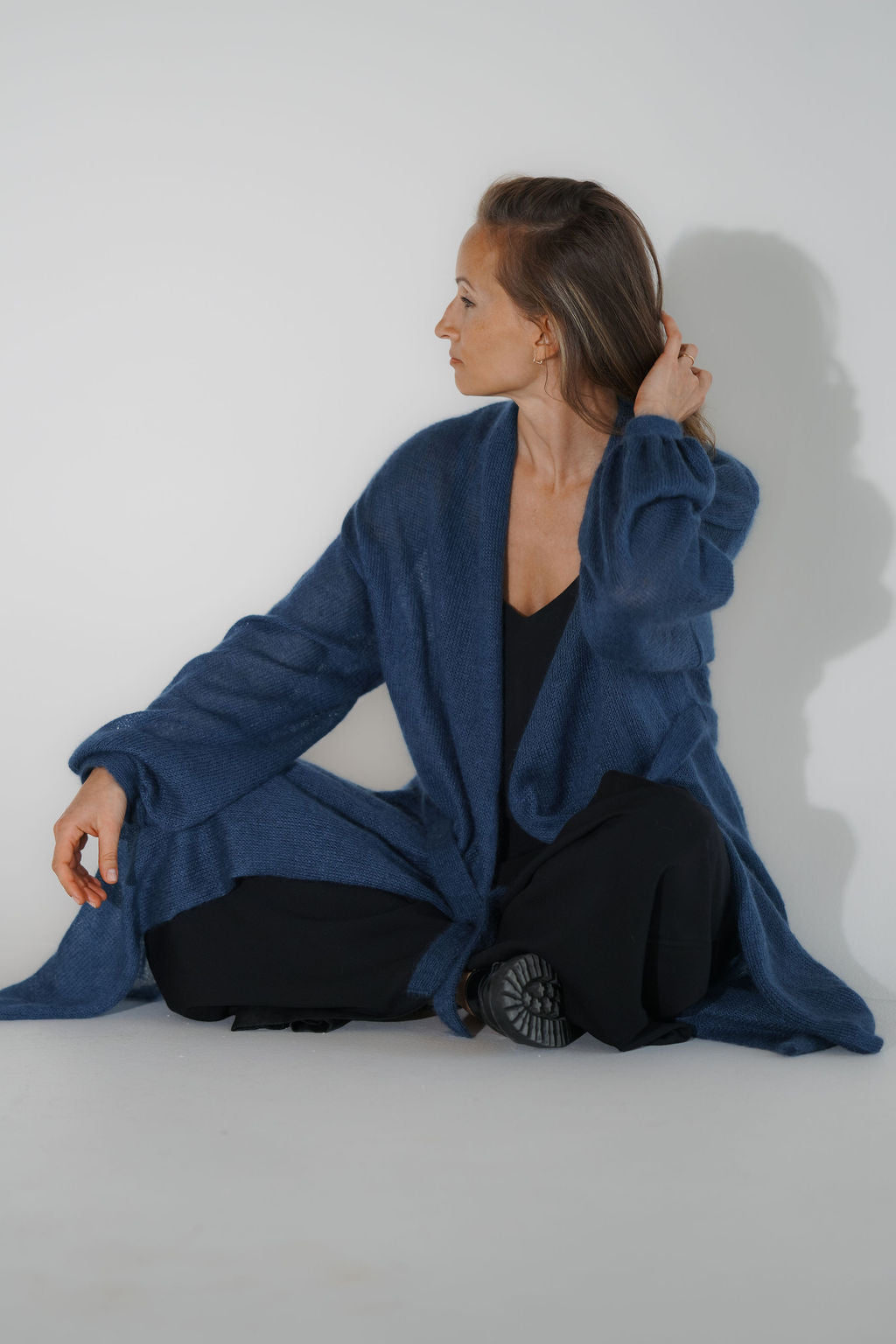 Seated woman in a knitted kid mohair and silk long cardigan with puff sleeves and belt